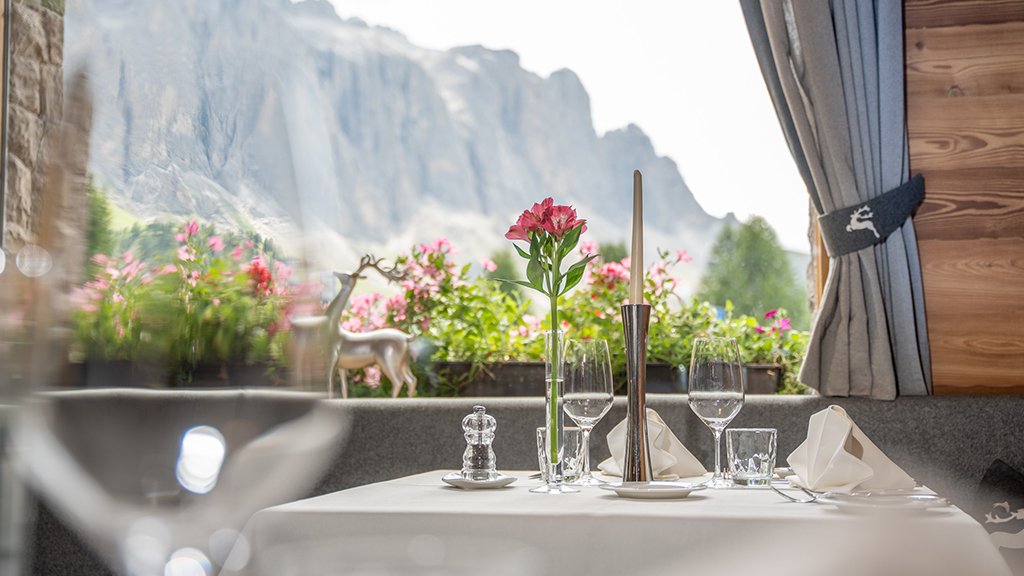 Elegantly set restaurant table with a view of the Sassolungo massif framed by curtains